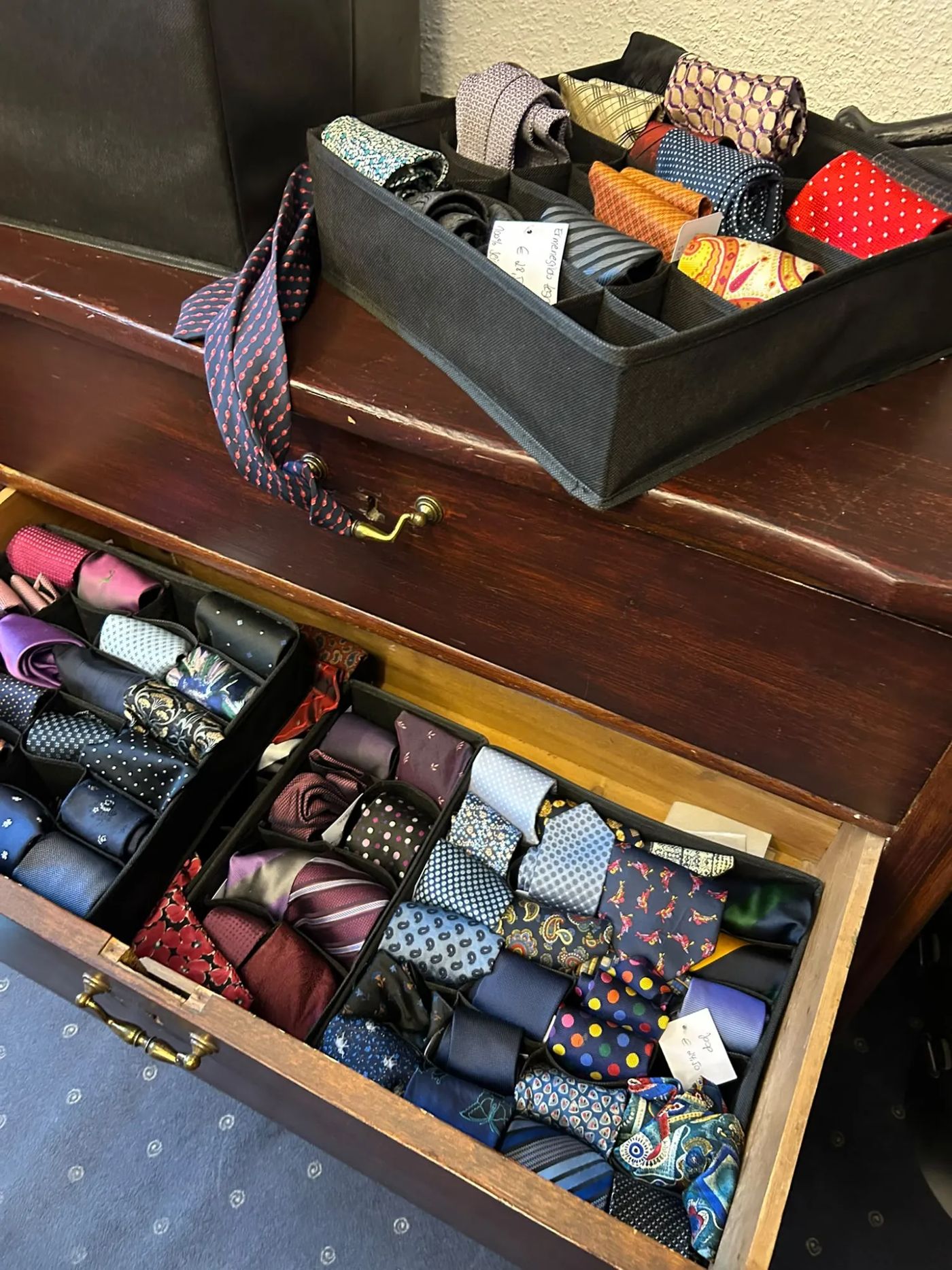 Offene Schublade einer alten Kommode, gefüllt mit aufgerollten Krawatten in Sortierboxen